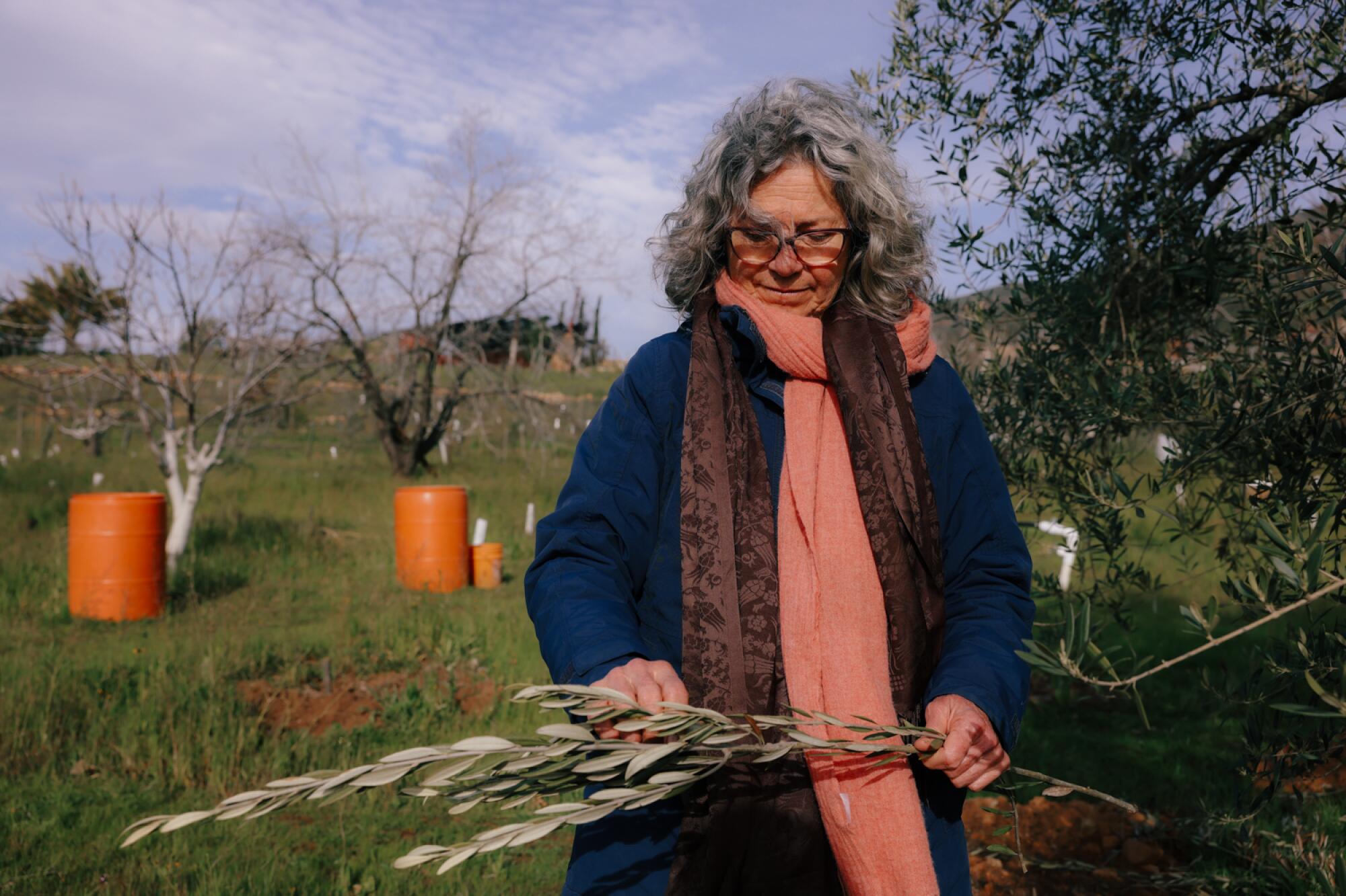 A woman stands outdoors and holds stalks of plants