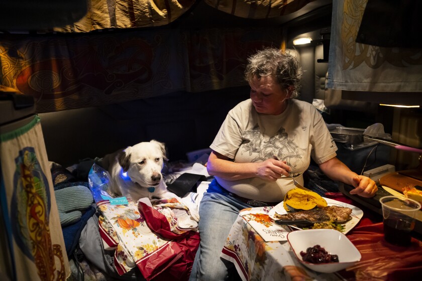 A trucker sits by her dog and enjoys her dinner in the cabin of her truck.