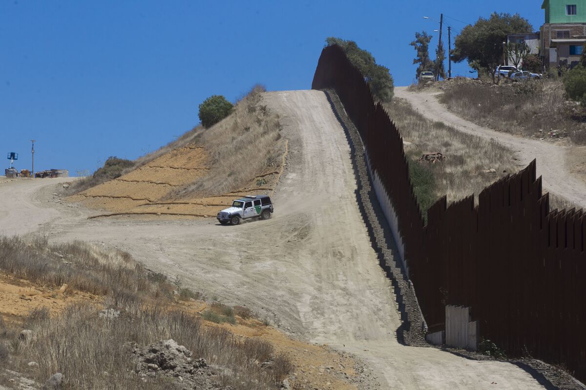 A Border Patrol vehicle patrols along a border fence. 