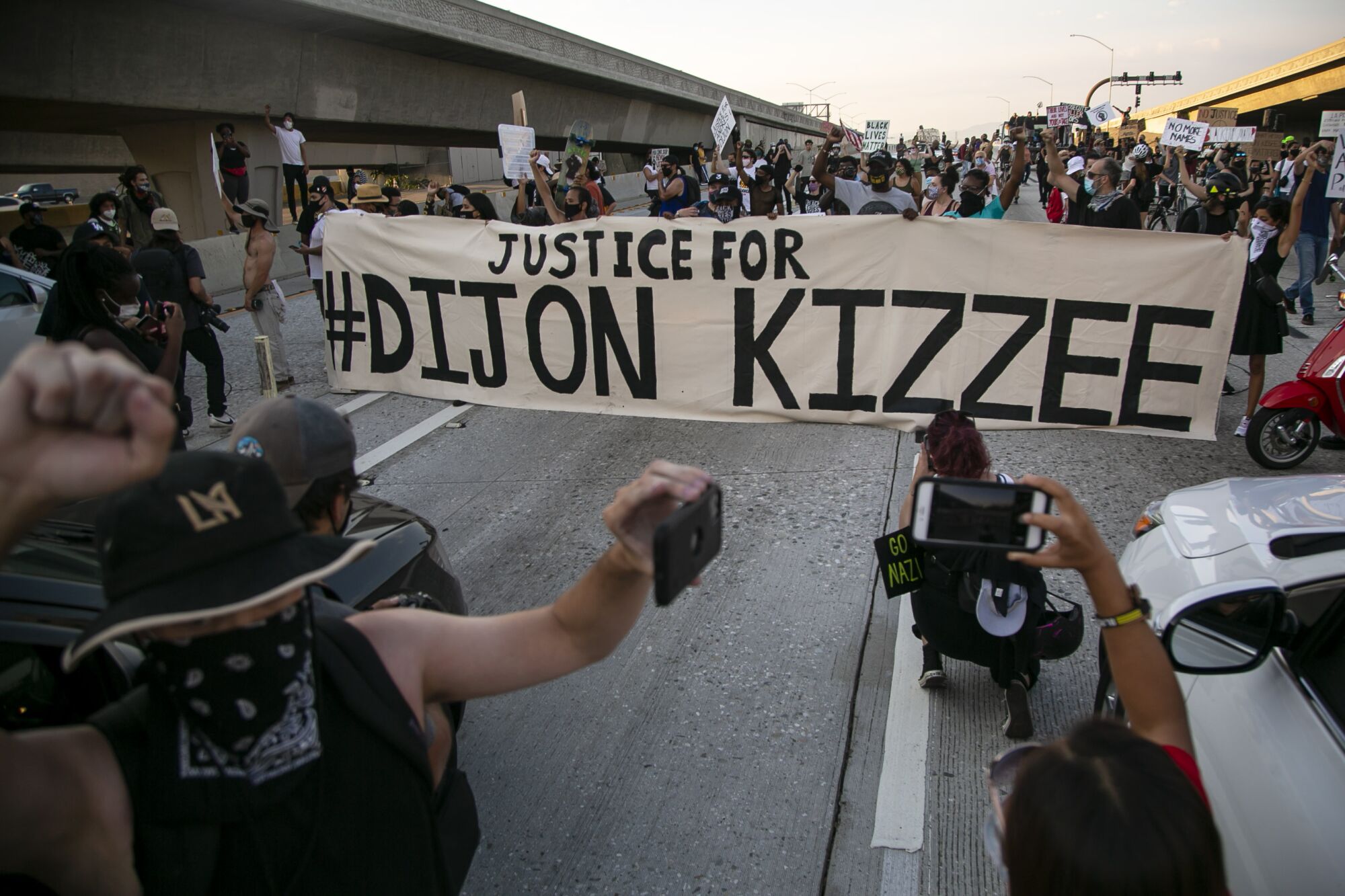 People on the freeway protest, holding a "Justice for #Dijon Kizzee" banner and shooting photos and film.