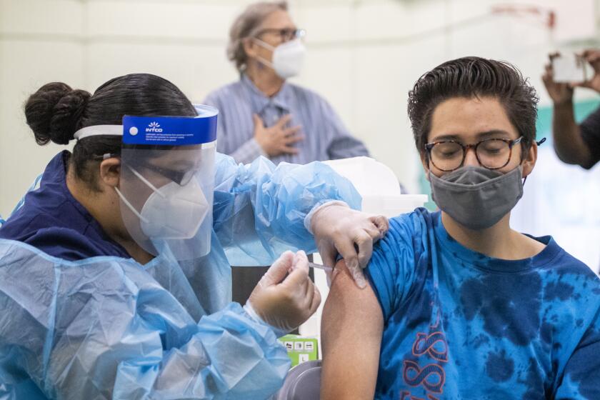 Eagle Rock, CA - August 30: Registered Nurse Priscilla V., left, gives a Pfizer-BioNTech vaccine shot to Dean Iida, 17, a senior at Eagle Rock High School, as Los Angeles County Board of Supervisors Chair Hilda Solis, Interim Superintendent Megan K. Reilly, School Board members Kelly Gonez and Jackie Goldberg and special guests visit Los Angeles Unified School-based mobile vaccination clinics at Eagle Rock High School on Monday, Aug. 30, 2021 in Eagle Rock, CA. All employees in the Los Angeles Unified School District must be vaccinated against COVID-19 by Oct. 15, an order that puts it at the forefront of school systems across the country that are mandating strict coronavirus safety measures for employees and students. (Allen J. Schaben / Los Angeles Times)