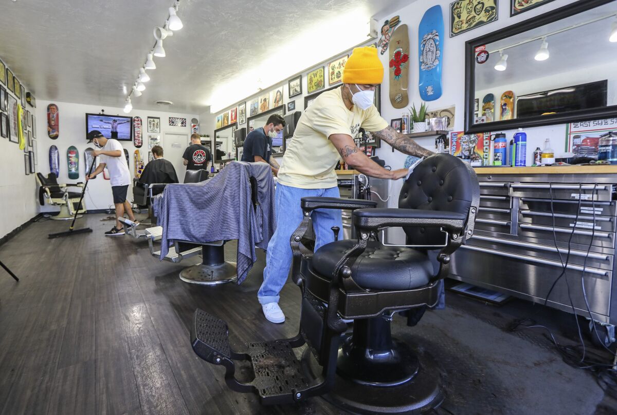 Maintaining hygiene rules, Leucadia Barber Shop manger Emiliano Zermeno (right) wipes down his barber chair