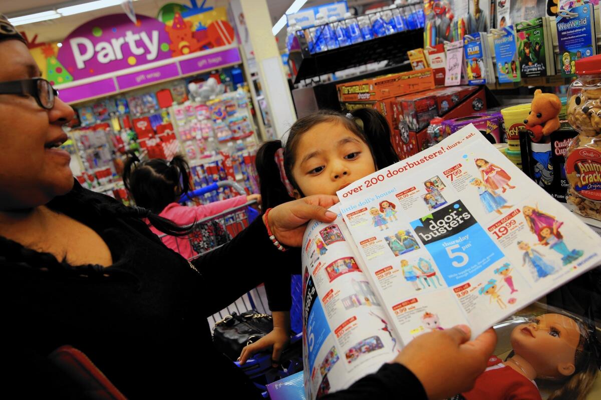 Makayla Guerrero, 5, peers over at the sales flier her mother, Laura Morales, of Los Angeles, shows a Toys R Us cashier at the checkout lane to confirm a sale item on Friday