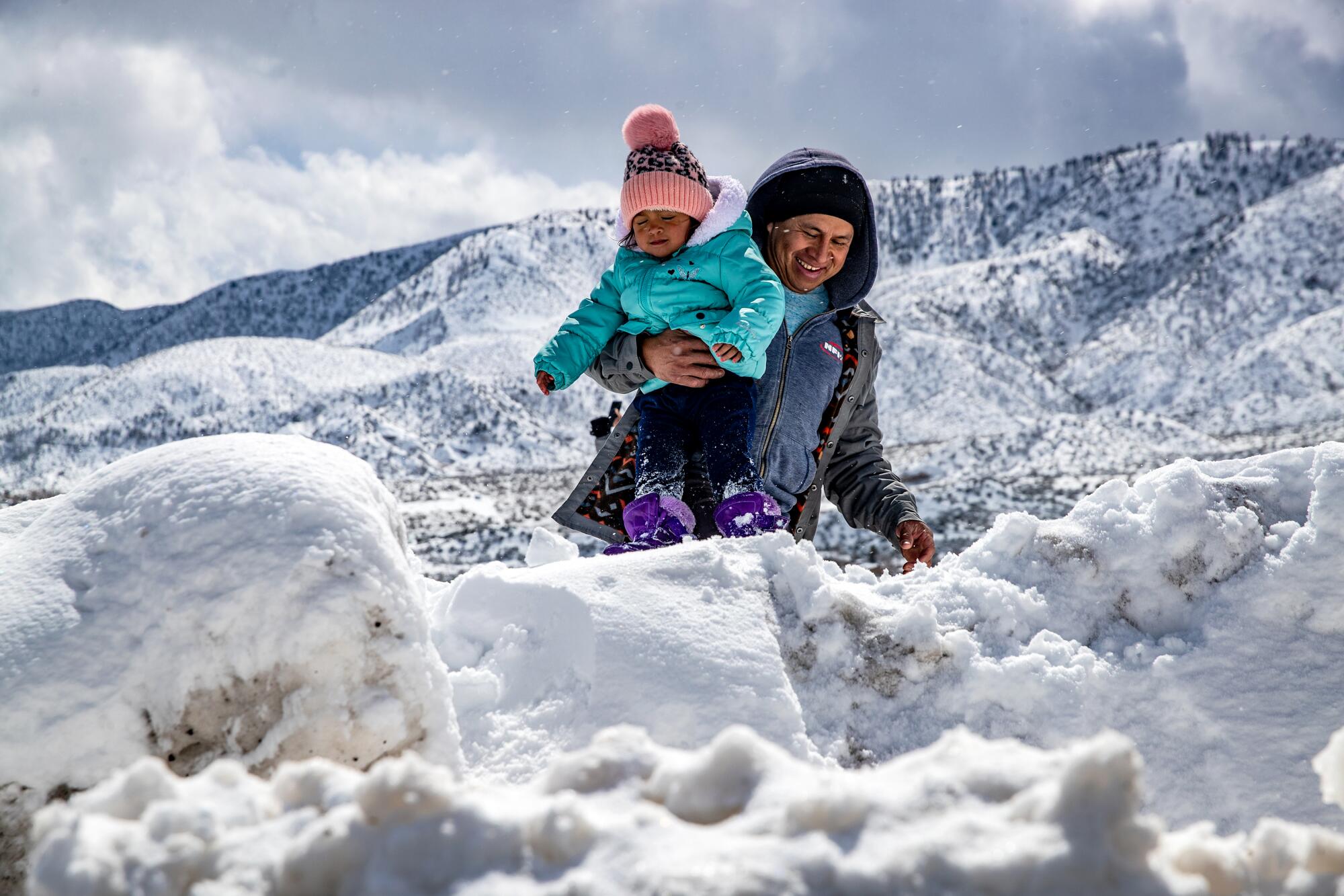 A man carries his toddler through snow in the mountains