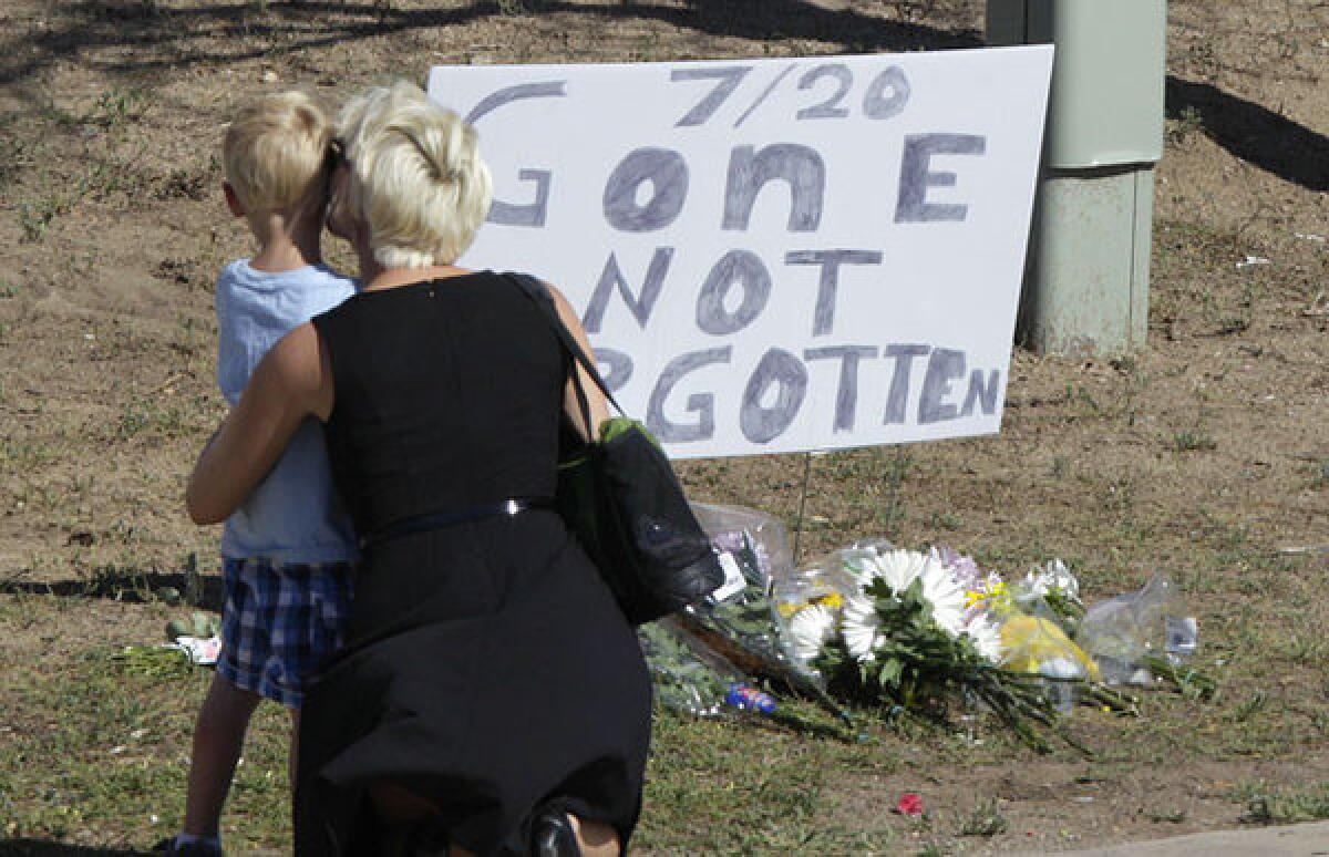 A woman and a child stand near a sign that reads, "7/20 Gone Not Forgotten," near the movie theater where a gunman killed at least 12 people and wounded dozens of others in Aurora, Colo.