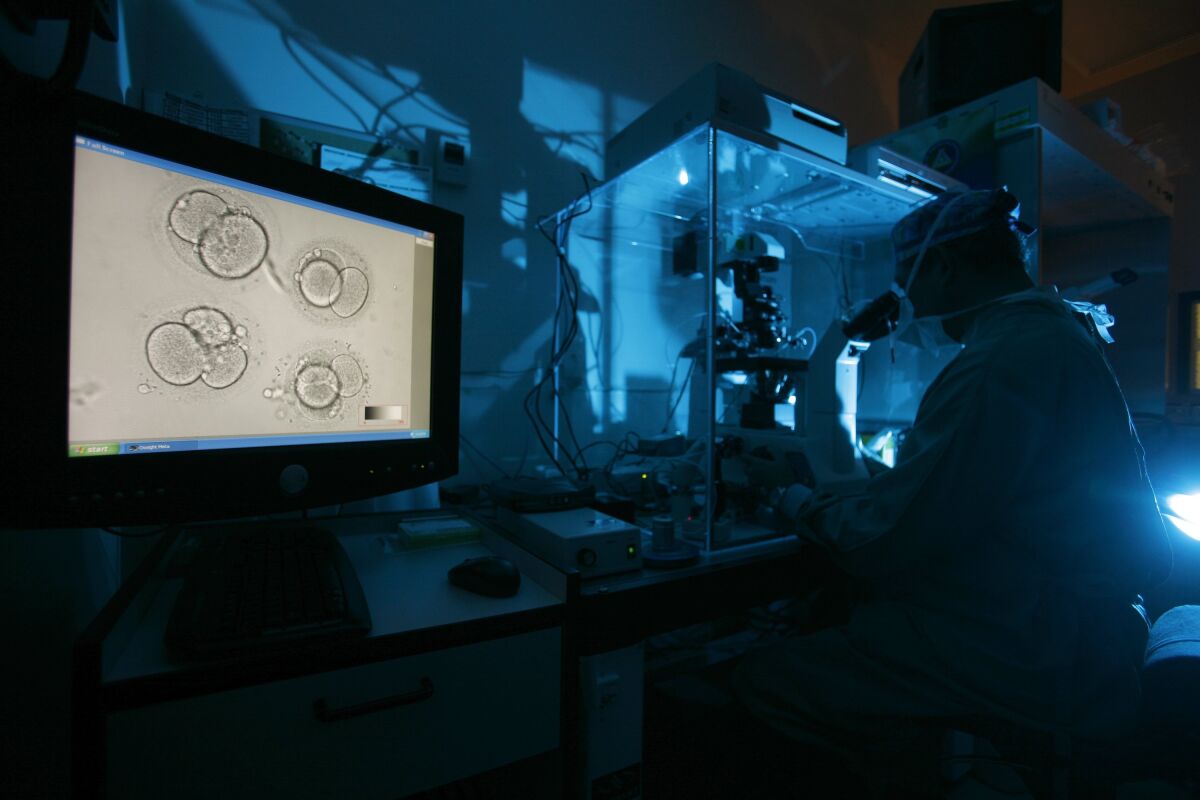 A person looks into a microscope in a blue-lighted room.