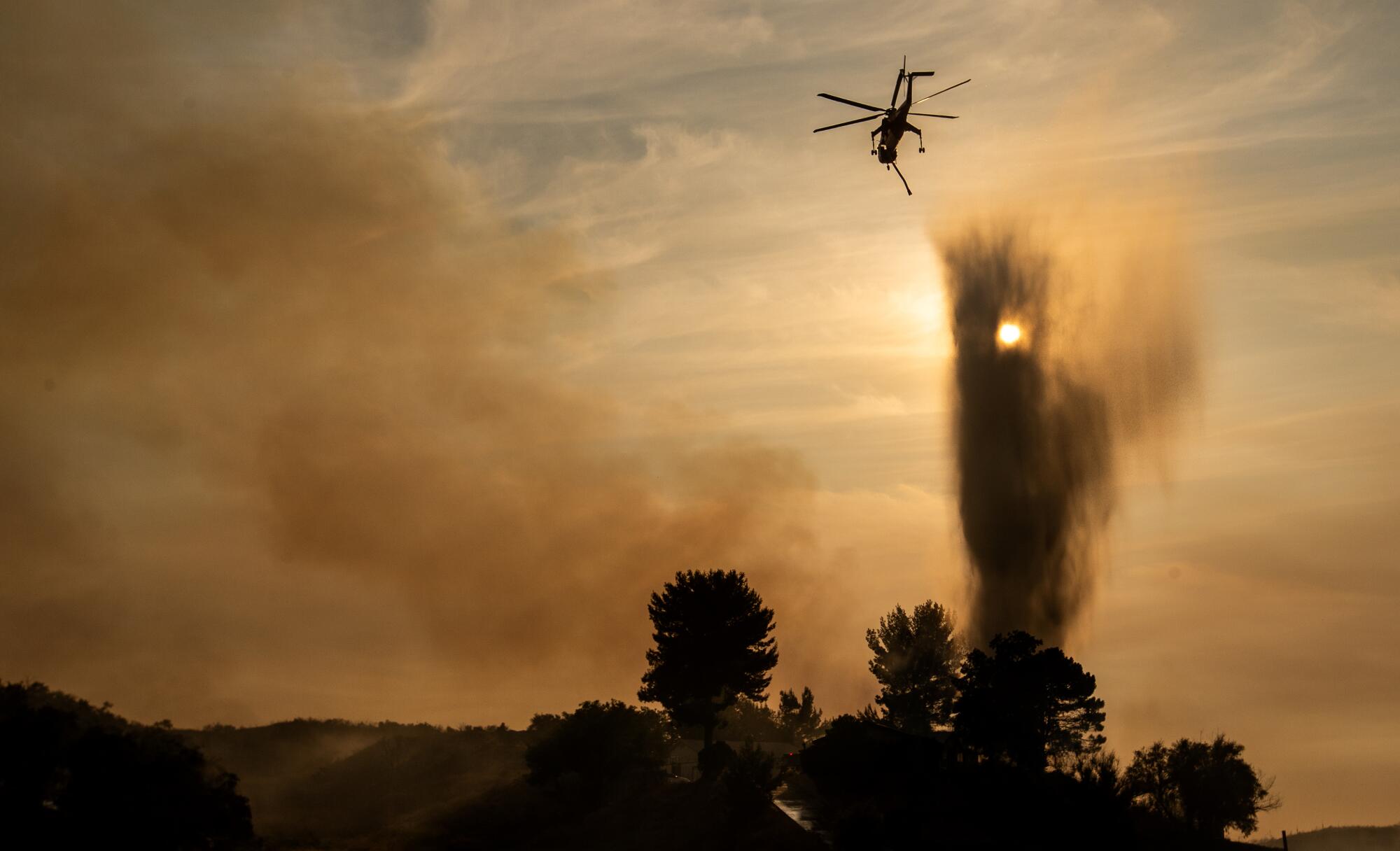 A helicopter is silhouetted against a smoky sky.