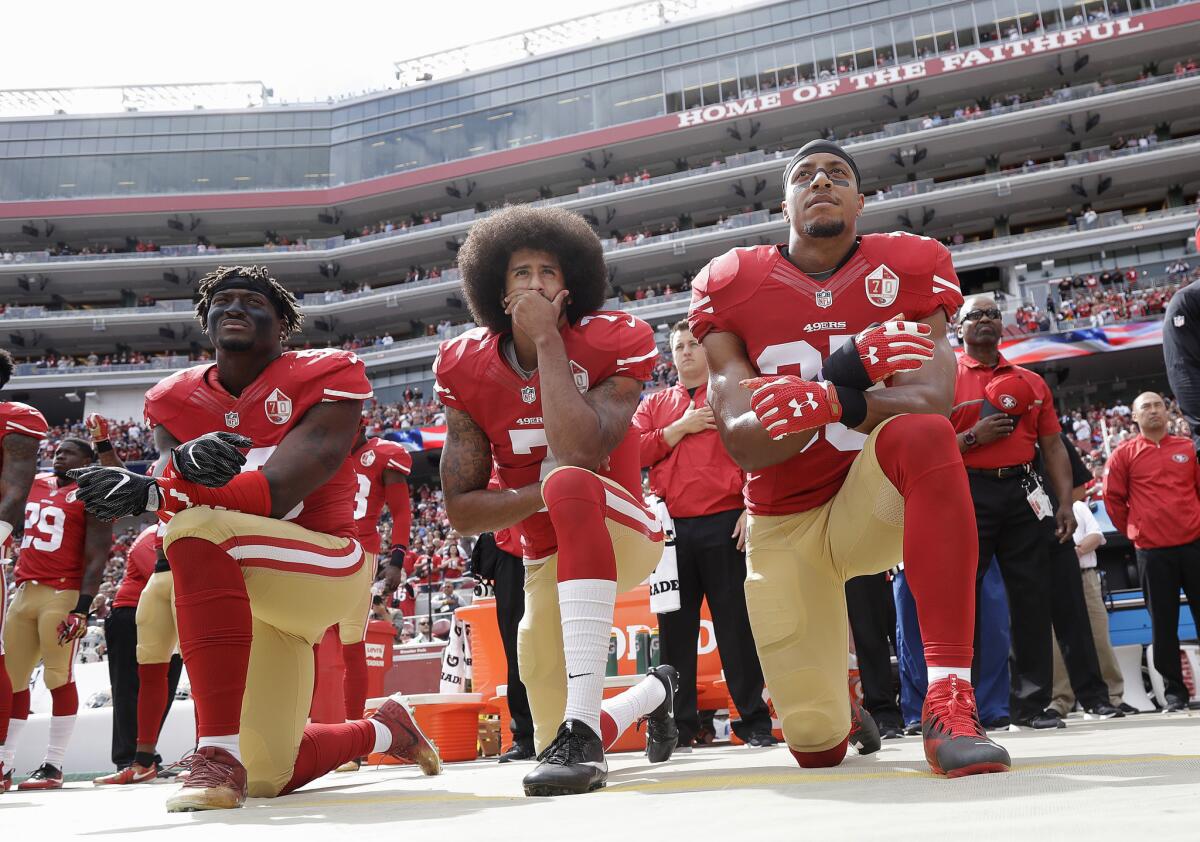 Eli Harold (i), Colin Kaepernick (c) y Eric Reid, hincados, en su protesta con el jersey de los 49ers, durante el himno de Estados Unidos.