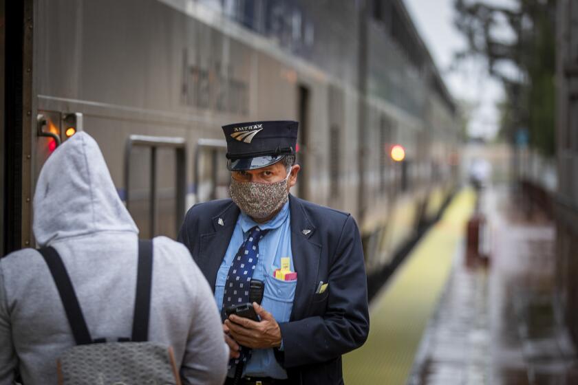 SANTA ANA, CA -- THURSDAY, APRIL 9, 2020: An Amtrak officer wears a protective mask while checking passengers boarding the train at the Santa Ana Regional Transportation Center amid coronavirus (COVID-19) physical distancing restrictions in Santa Ana, CA, on April 9, 2020. (Allen J. Schaben / Los Angeles Times)