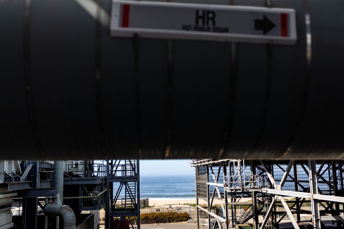 From a power plant, past pipes and stairs, the beach and ocean are visible.