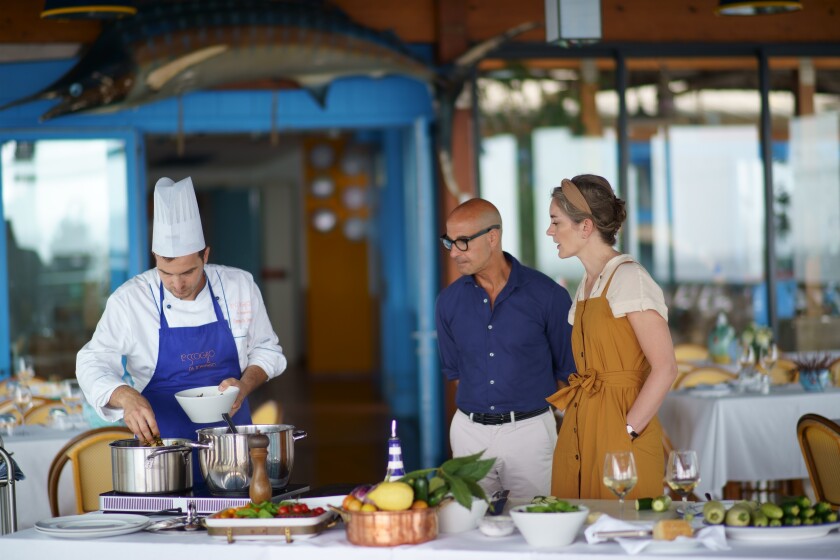 Stanley Tucci and wife Felicity Blunt watch as a chef prepares a meal.
