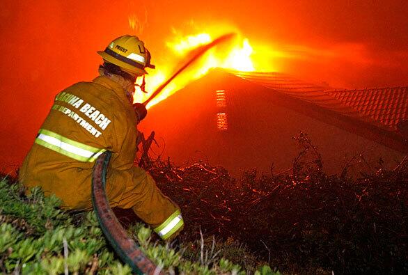 A firefighter aims a stream of water at a home on Olinda Drive in Brea. Strong winds blew through the Carbon Canyon area and drove embers into the attic. This home and the house next door were lost to the fire.