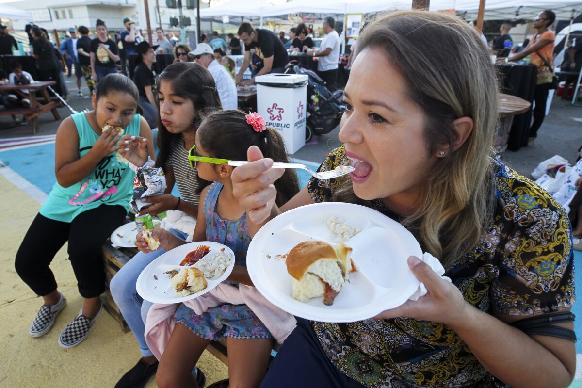 Jenny Ruiz and her children, from left, Natalie Ruiz, 10, Bella Ruiz, 12, and Gabby Ruiz, 6, eat pulled pork sandwiches from Rick's Grill food booth during the City Heights Street Food Festival on Thursday , September 12, 2019 in San Diego, California .