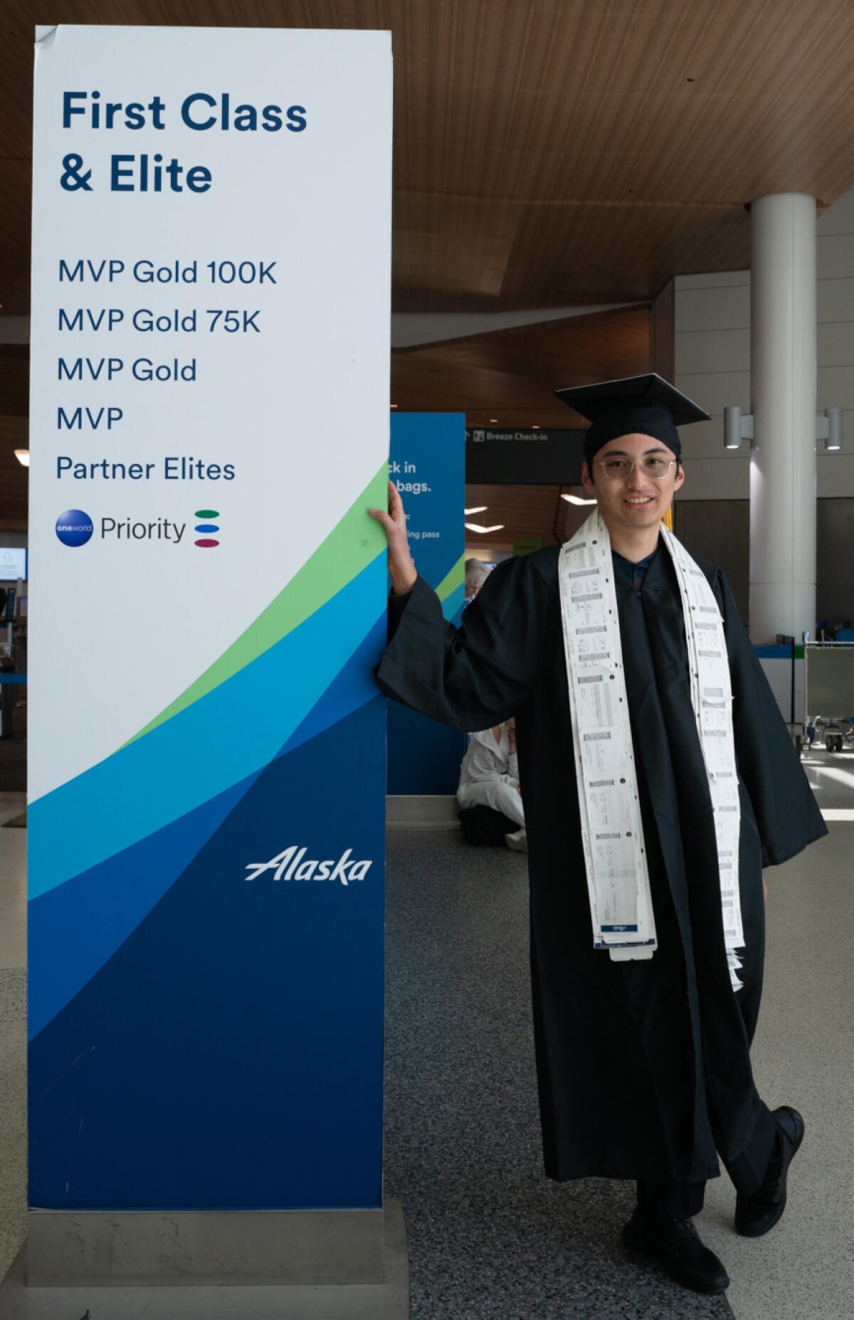 Bill Zhou, pictured in graduation garb next to an Alaska Airlines sign.