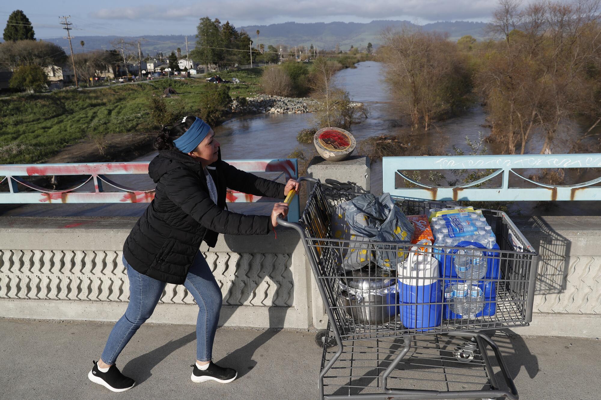 A woman shoves a shopping cart of supplies over the Pajaro River Bridge