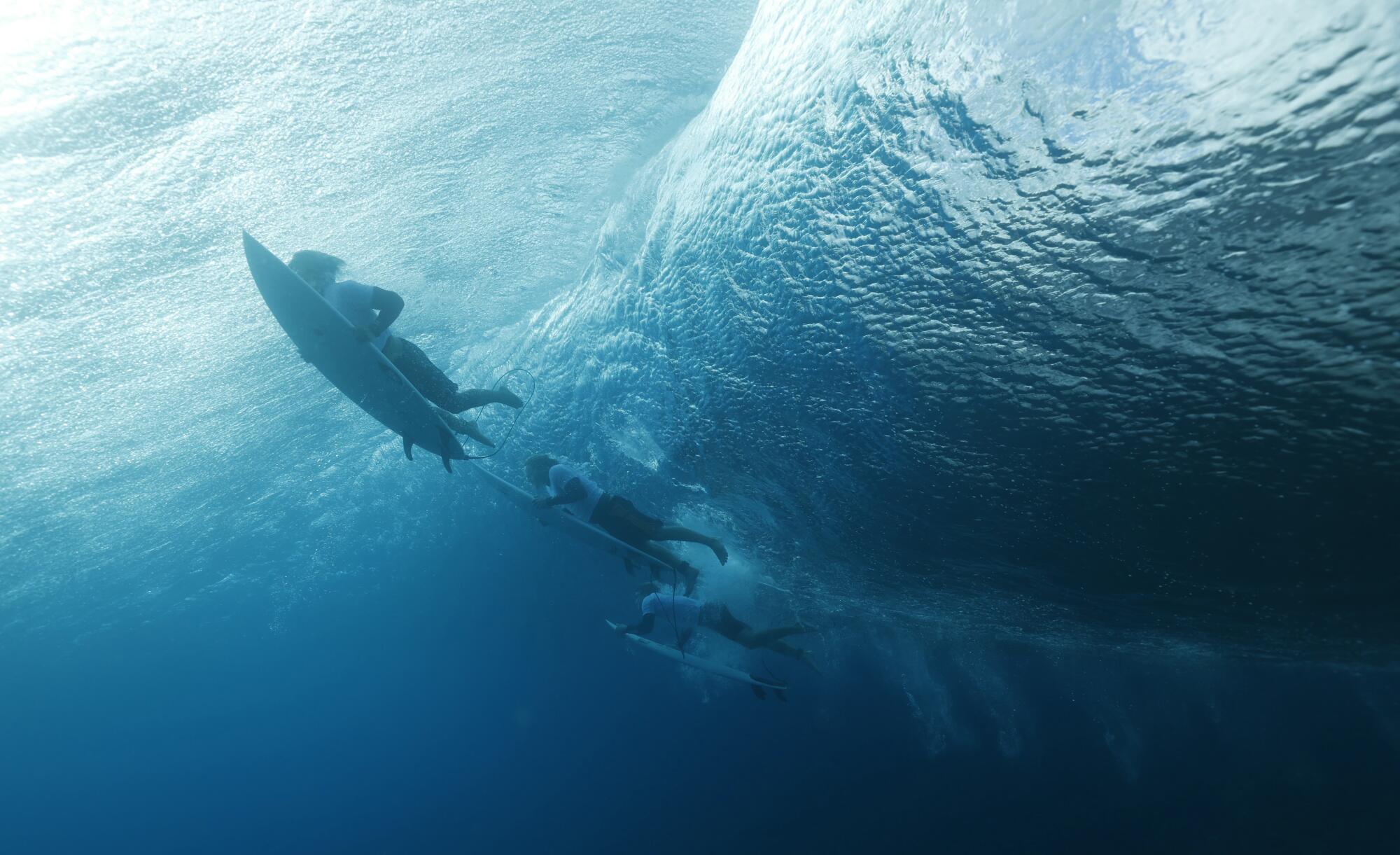 An underwater view of surfers paddling out to sea. 
