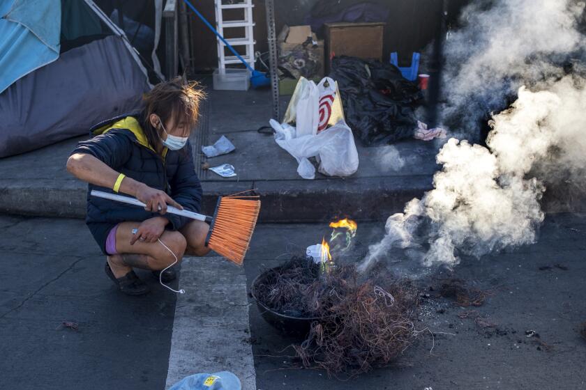 Los Angeles, CA - December 09: Toxic smoke billows up over a line of tents on the sidewalk as a person burns the plastic off copper wires in skidrow on Friday, Dec. 9, 2022, in Los Angeles, CA. They were using a broom the fan the flames. (Francine Orr / Los Angeles Times)