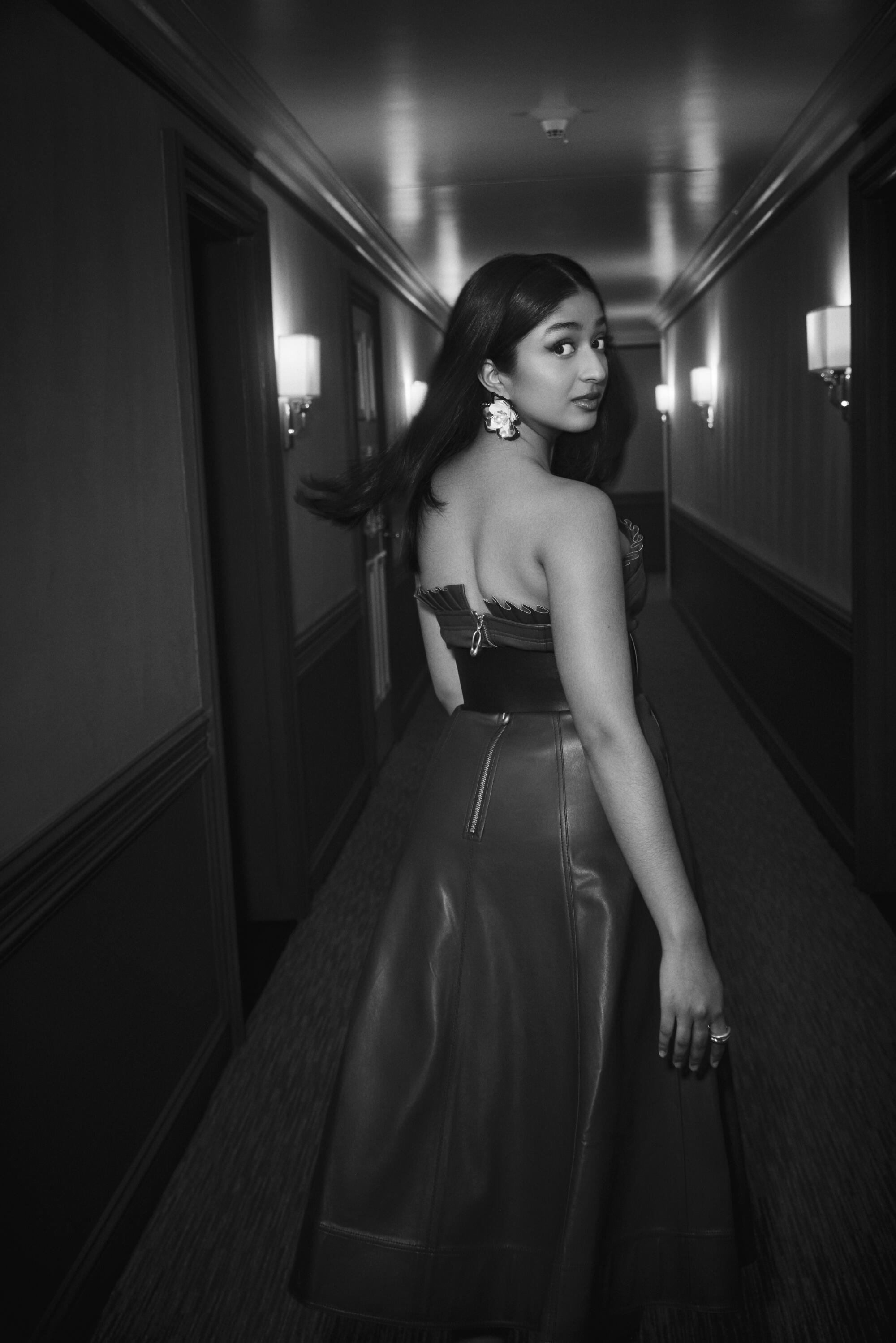 In a black-and-white photo, Maitreyi Ramakrishnan stands in a hotel hallway and looks back over her right shoulder.