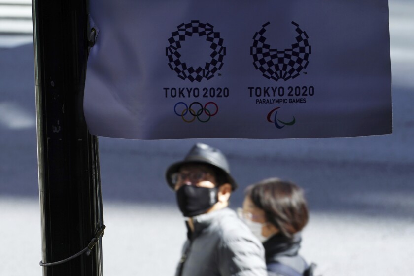 People wearing protective masks to help curb the spread of the coronavirus walk near a banner of Tokyo 2020 Olympic and Paralympic Games Wednesday, March 3, 2021, in Tokyo. The Japanese capital confirmed more than 310 new coronavirus cases on Wednesday. (AP Photo/Eugene Hoshiko)