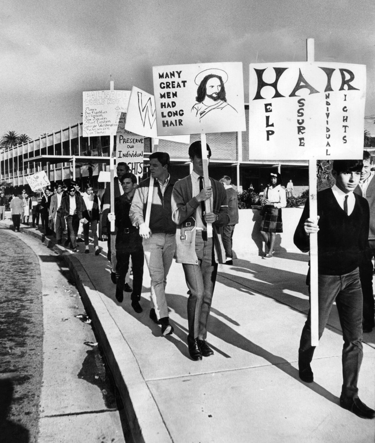 a black and white photo of high school boys carrying signs in support of long hair