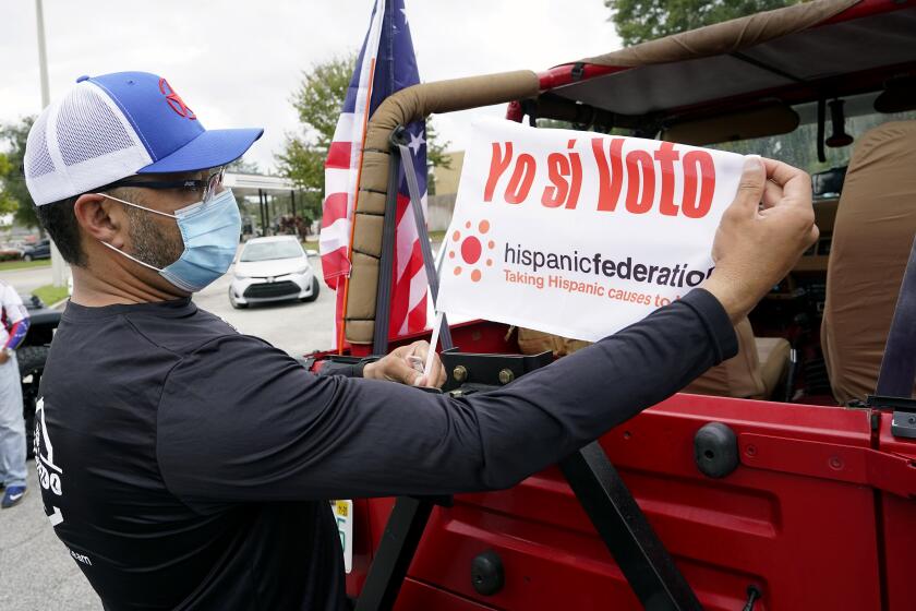 John Gimenez attaches a flag to his vehicle during an event hosted by the Hispanic Federation to encourage voting in the Latino community Sunday, Nov. 1, 2020, in Kissimmee, Fla. The Hispanic Federation is a non-partisan organization. (AP Photo/John Raoux)