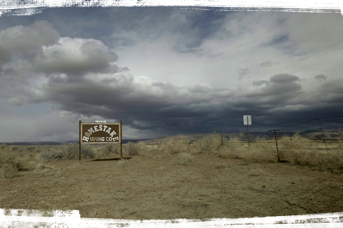 A sign reading "Homestake Mining Co" standing in the desert near a fence