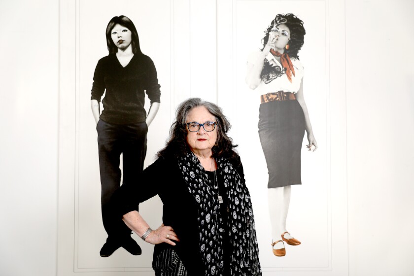 هنرمند جودی بوکا در مقابل دو تصویر از زنان روی دیوار ایستاده است.