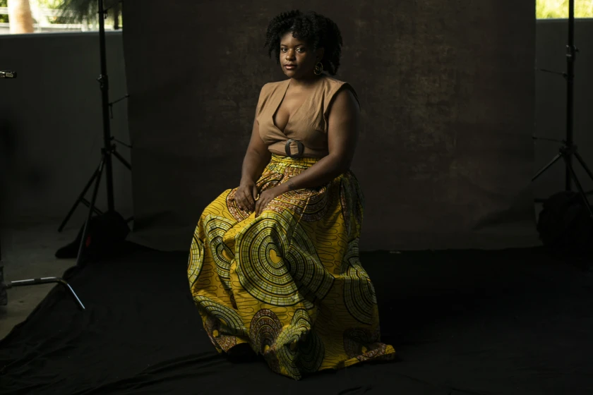 Olympia Auset sits solemnly in a photography studio