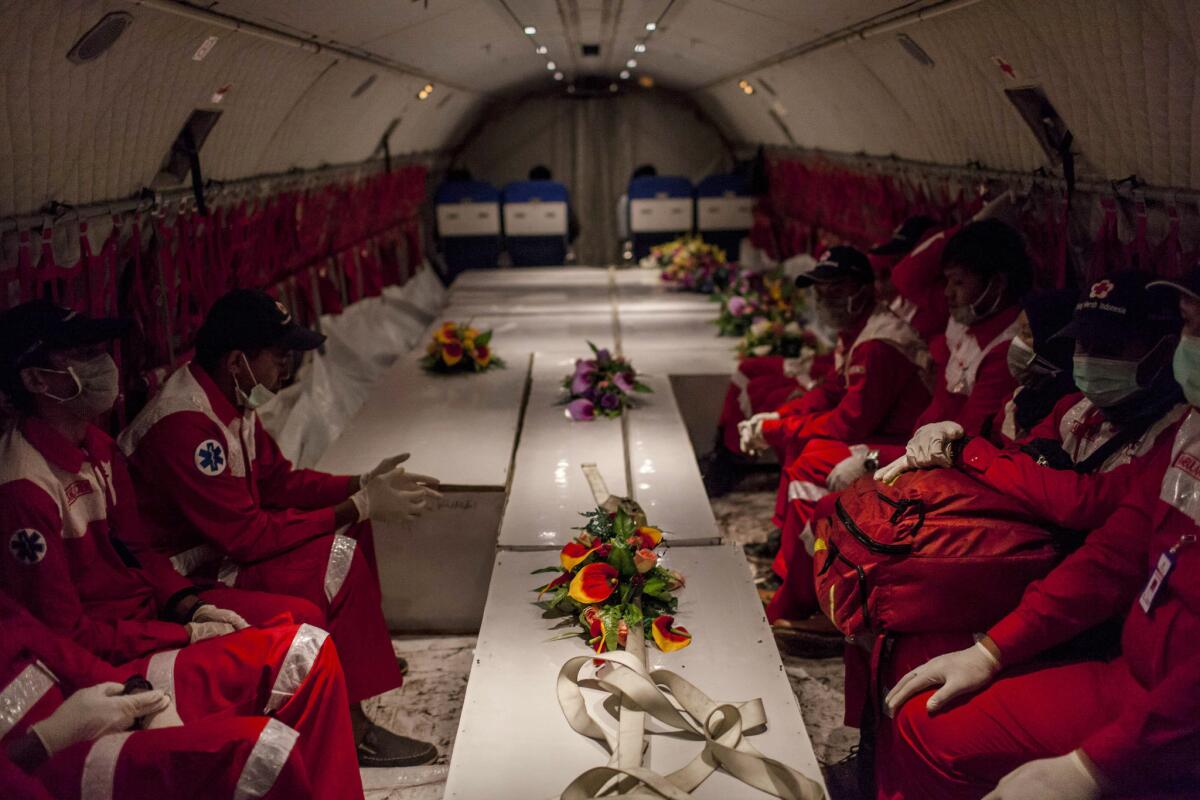 Members of the Indonesian Red Cross aboard an Indonesian air force aircraft watch over 10 coffins containing bodies of AirAsia Flight 8501 crash victims.