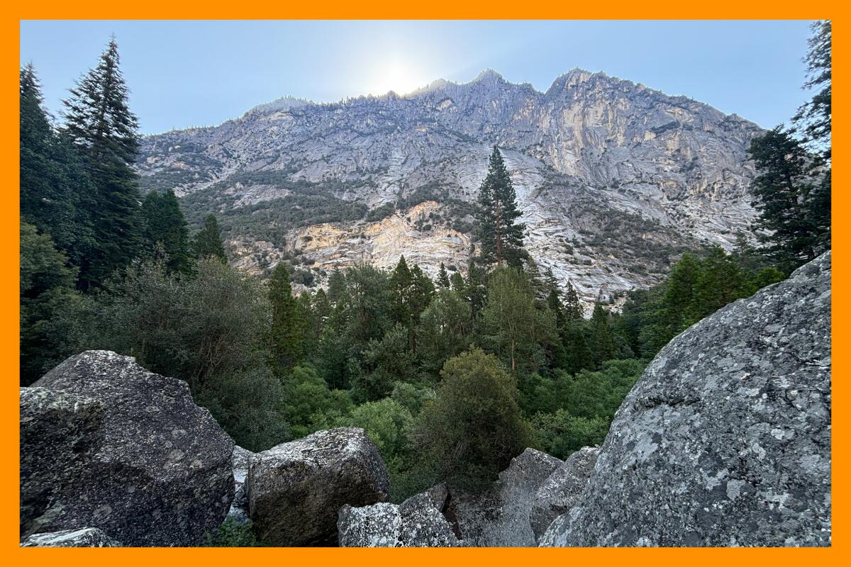 Boulders and trees sit at the base of a massive rocky mountain.