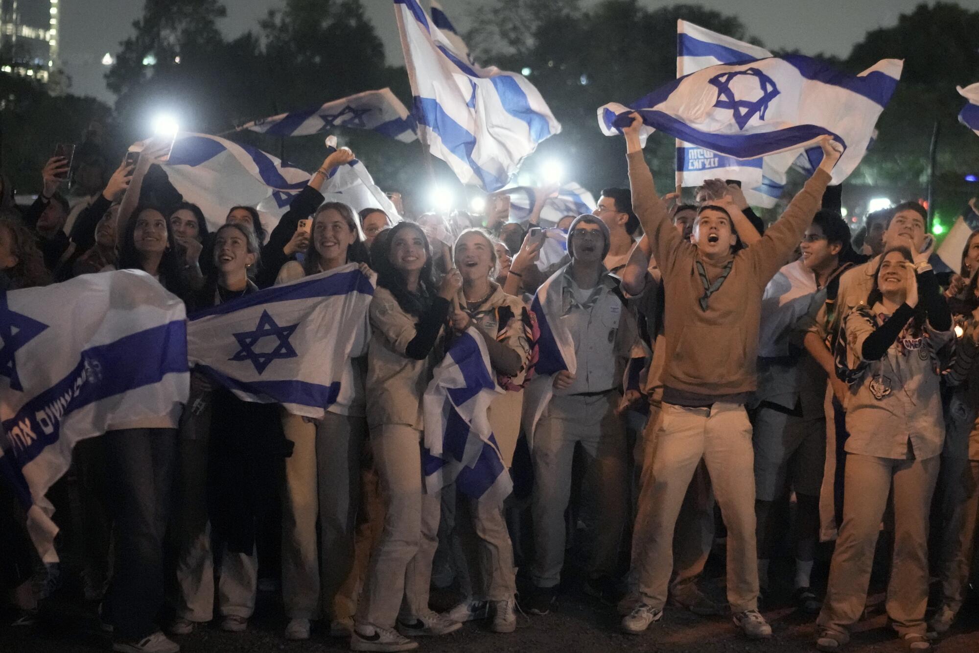 People celebrate and hold up Israeli flags.