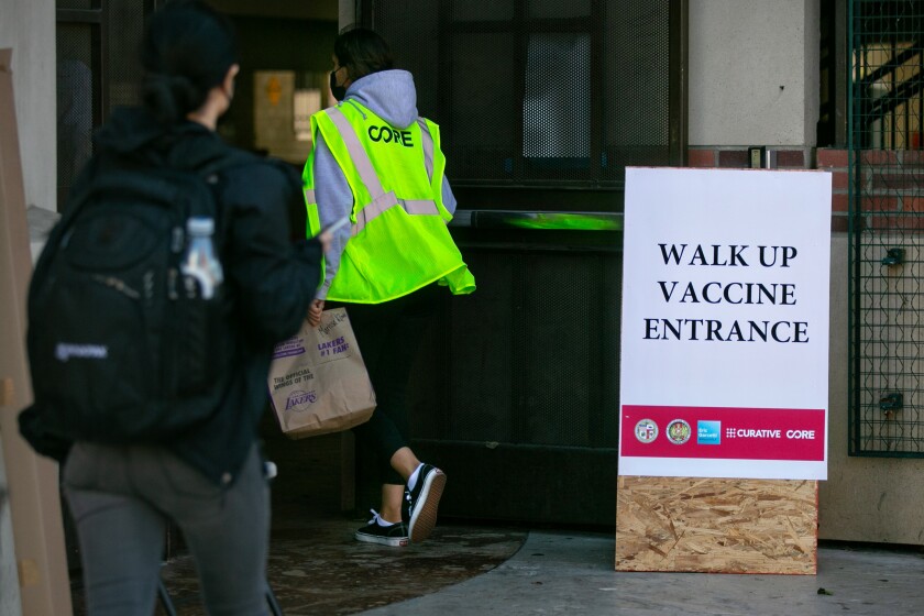 A person in a high-vis vest walks past a sign that says Walk up vaccine entrance