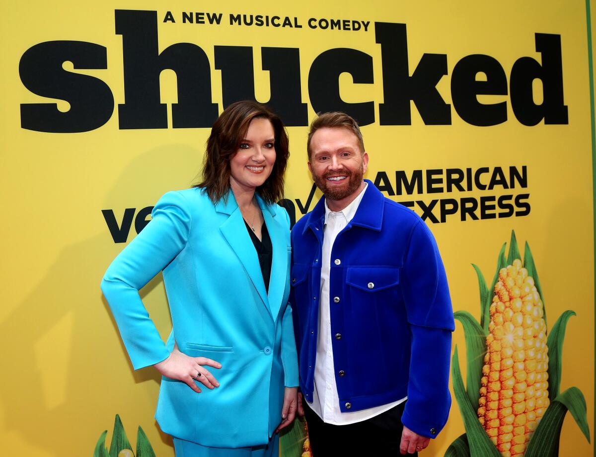 Two people stand in front of a Broadway poster