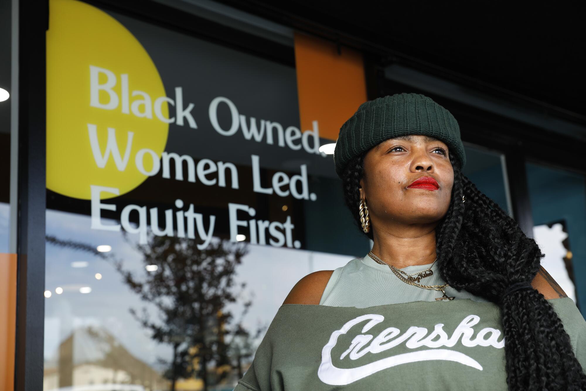 Kika Keith stands outside her business' front window, which has a sign that reads, "Black Owned. Women Led. Equity First."
