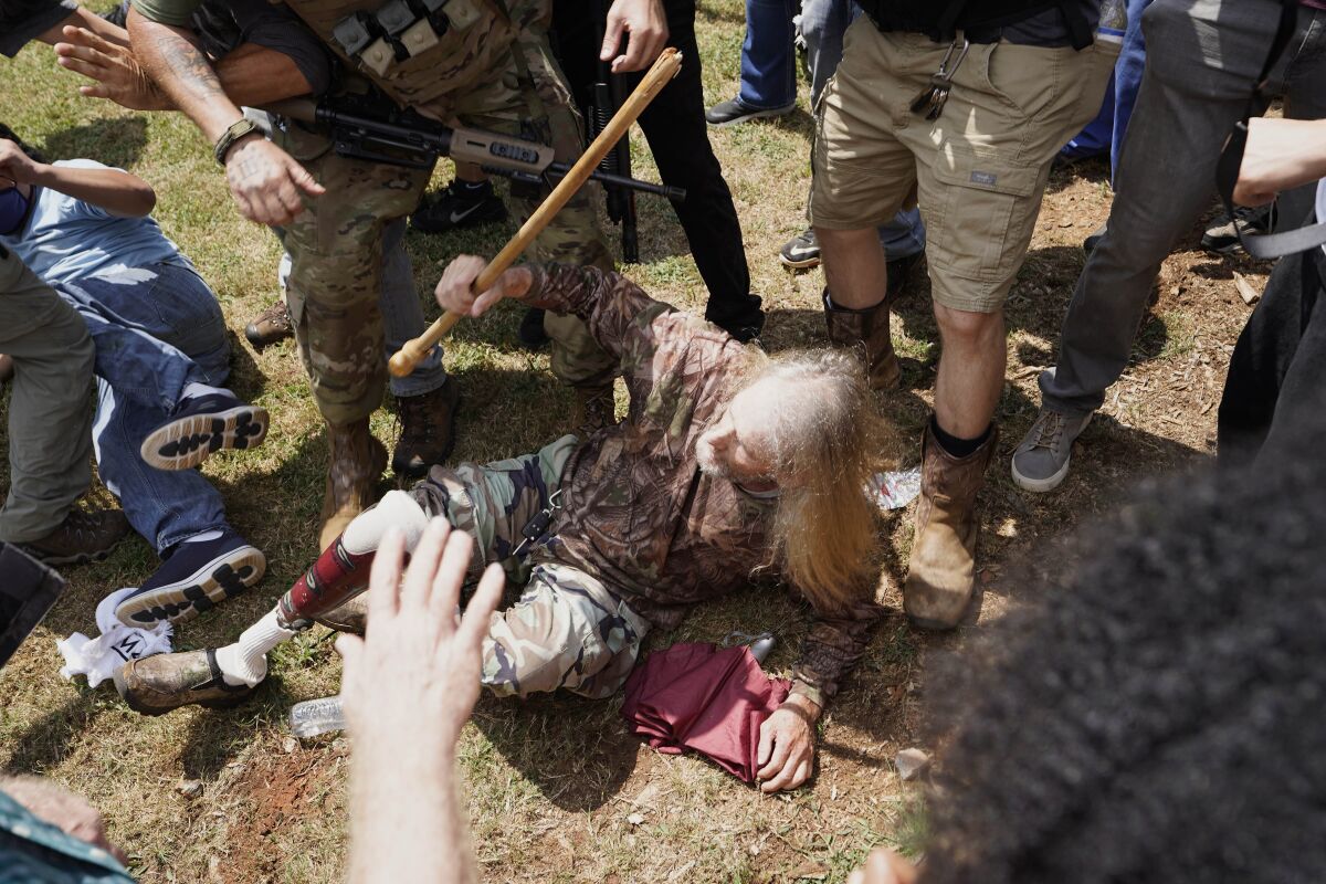 A man falls after being hit by counter demonstrators during a protest , Saturday, Aug. 15, 2020, in Stone Mountain Village, Ga. Several dozen people waving Confederate flags, many of them wearing military gear, gathered in downtown Stone Mountain where they faced off against a few hundred counterprotesters, many of whom wore shirts or carried signs expressing support for the Black Lives Matter movement. (AP Photo/John Bazemore)