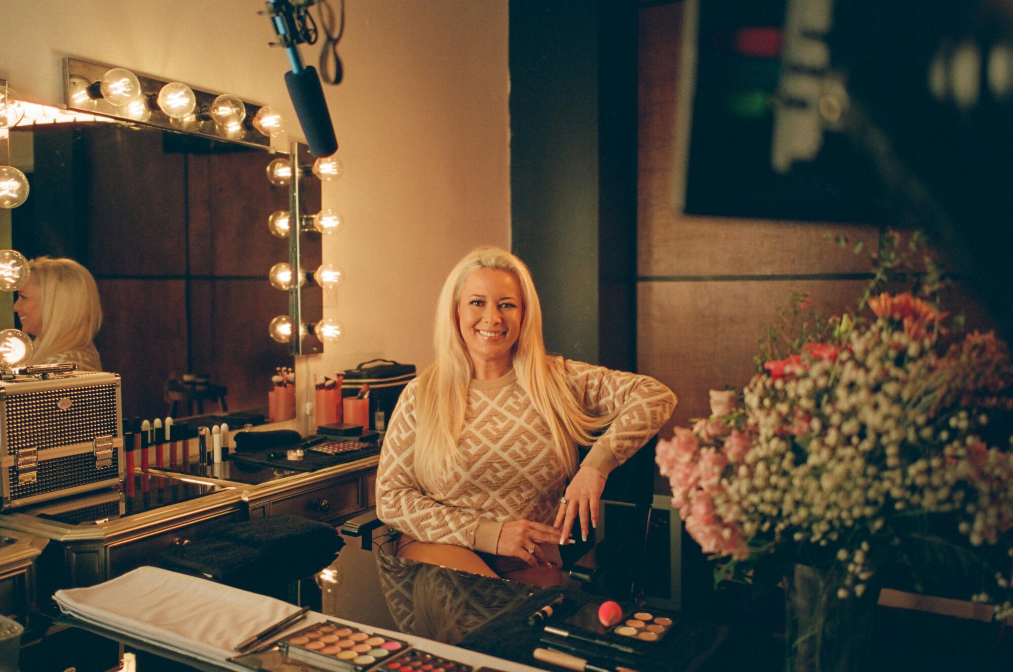 Katrina Johnson, a blond woman, sits in a makeup chair on set. 