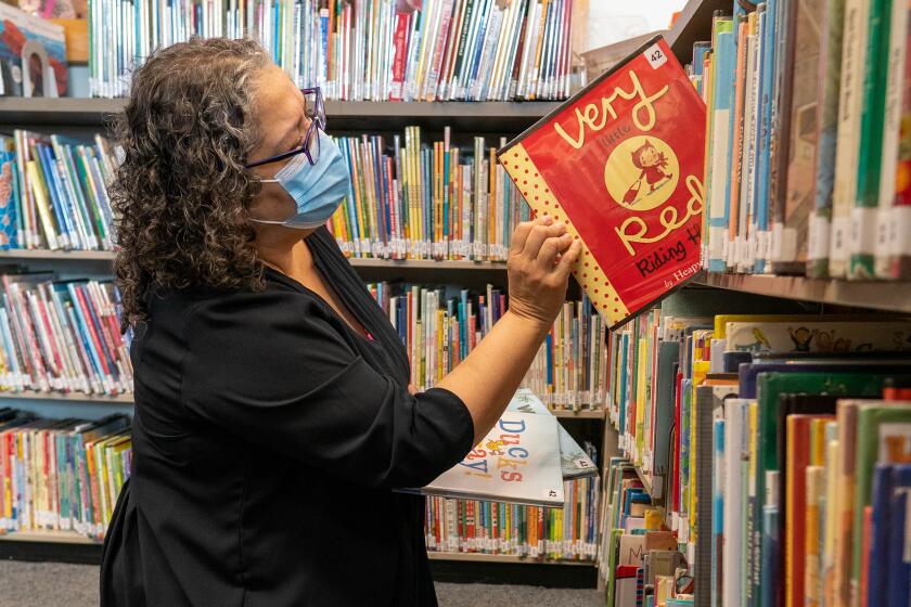 Una mujer saca un libro de un estante de la biblioteca en una sucursal de la Biblioteca Pública de Los ngeles.
