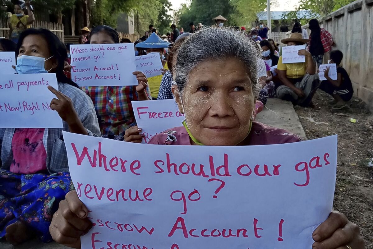 In this photo provided by Nwe Oo Tawlanyae Latpantaung, women sit in protest in the village of Latpantaung in Myanmar on Oct. 28, 2021, while holding signs calling for the freezing of revenues the Myanmar military gets from the sale of oil and gas. As the military's abuses have grown after seizing power in February, people from Myanmar's southern jungles to its northern mountains are voicing support for targeted sanctions on oil and gas funds, the country's single largest source of foreign currency revenue. (Courtesy of Nwe Oo Tawlanyae Latpantaung via AP)
