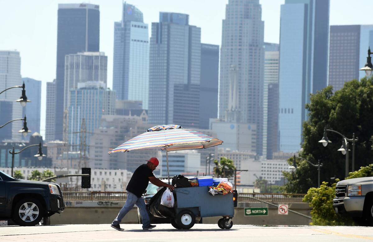A street vendor pushes a food cart with downtown L.A. as the backdrop.