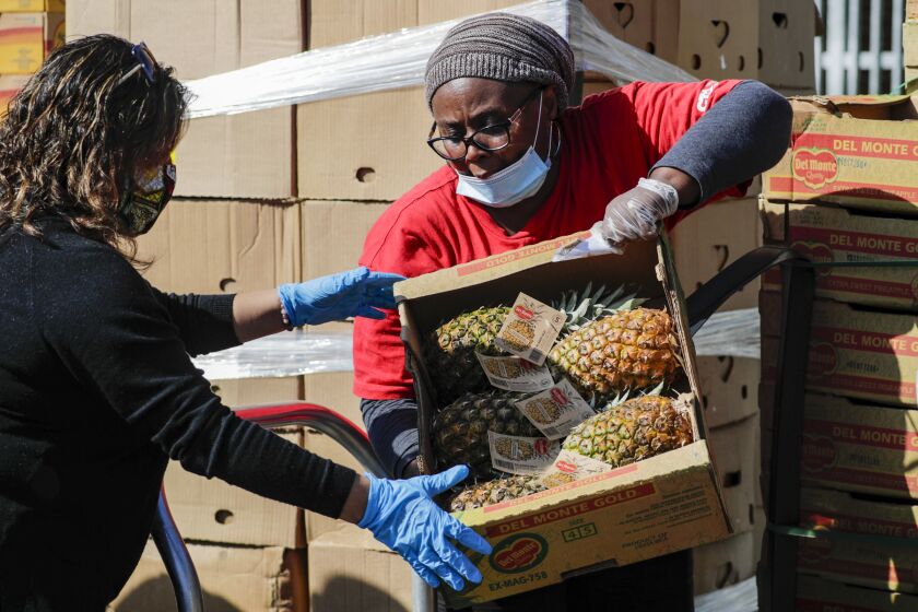 INGLEWOOD, CA - APRIL 04, 2020 -Aba Ngissah, a 6th grade teacher, right, and one other teacher unload fruits and vegetables for meal bags at Hudnall Elementary School in Inglewood. (Irfan Khan / Los Angeles Times)
