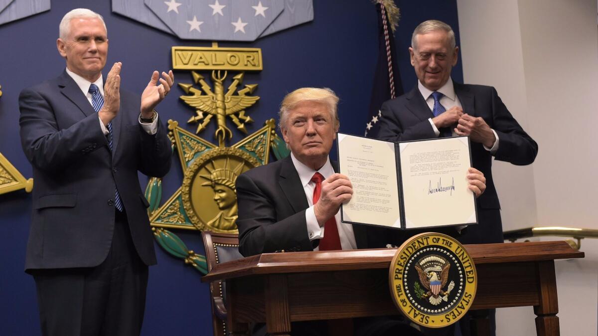 President Trump, flanked by Vice President Mike Pence, left, and Secretary of Defense James Mattis, shows his signature on executive orders signed Jan. 27. One of the orders banned people from seven predominantly Muslim nations from traveling to the United States.