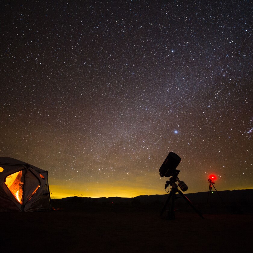 A tent and telescope silhouetted against a starry sky