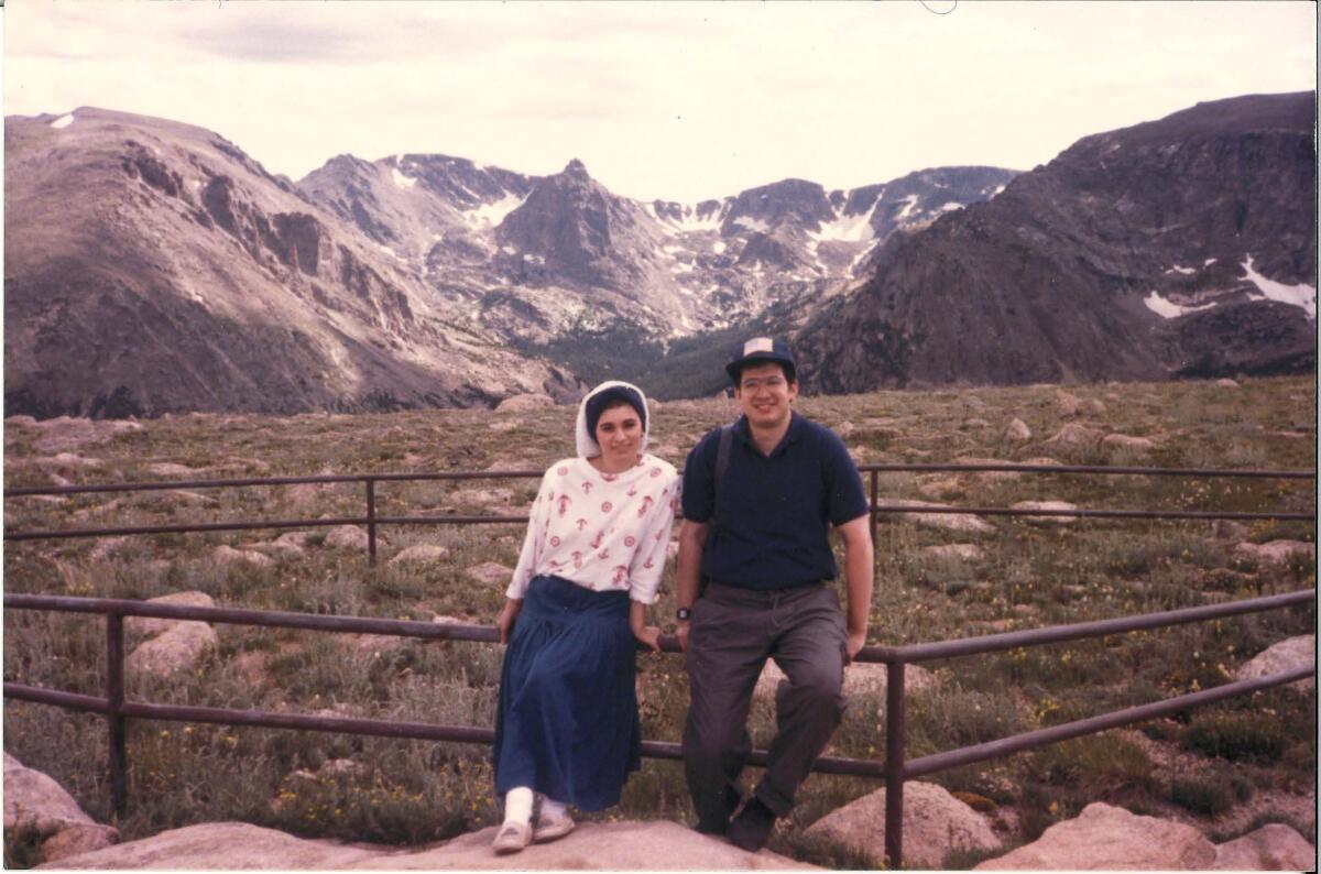 A woman wearing a head covering and a long skirt poses for a picture with a mountain in the background