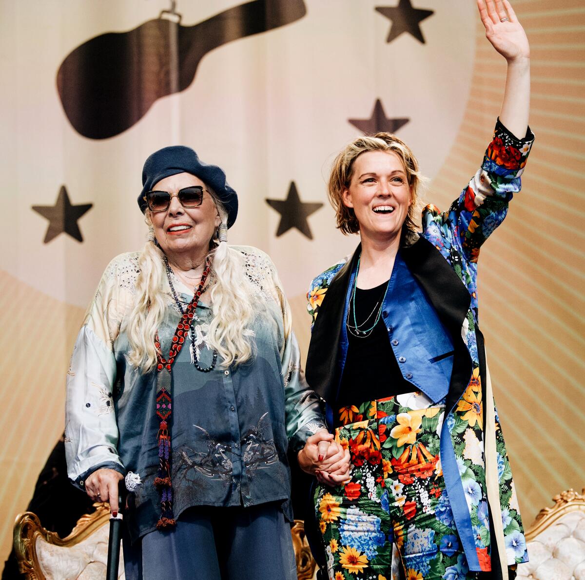Two women holding hands and smiling onstage together
