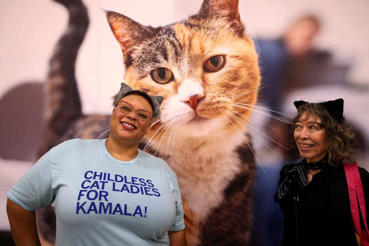 Two women stand in front of a giant photo of a cat.