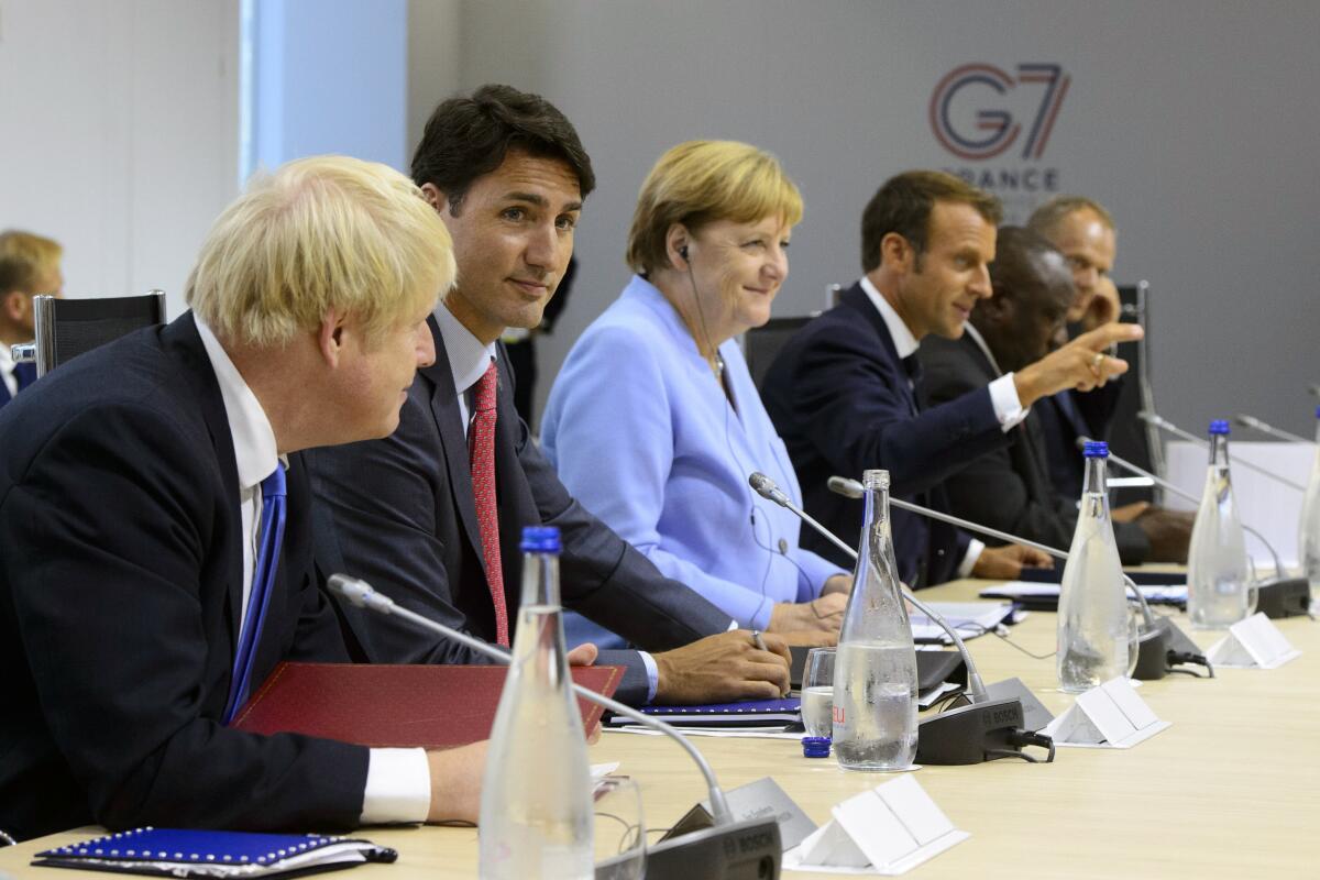 FILE - In this Aug. 26, 2019, file photo Canadian Prime Minister Justin Trudeau, second from left, sits between British Prime Minister Boris Johnson, left, and German Chancellor Angela Merkel as they take part in a meeting at the G7 Summit in Biarritz, France. Gesturing at right is French President Emmanuel Macron. It's a very exclusive club, perhaps the most selective in the world. Its current board members are Angela, Boris, Emmanuel, Justin, Mario, Yoshihide, and relative newcomer Joe. And they will be meeting this week after four years of U.S. disruption and a two-year coronavirus interruption. (Sean Kilpatrick/The Canadian Press via AP, File)