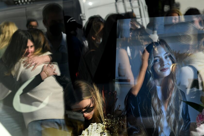 Los Angeles, California January 19, 2022: A picture of Croft House employee Brianna Kupfer sits inside the business as mourners are reflected in the window during a memorial at the Hancock Park furniture store Wednesday. (Wally Skalij/Los Angeles Times)