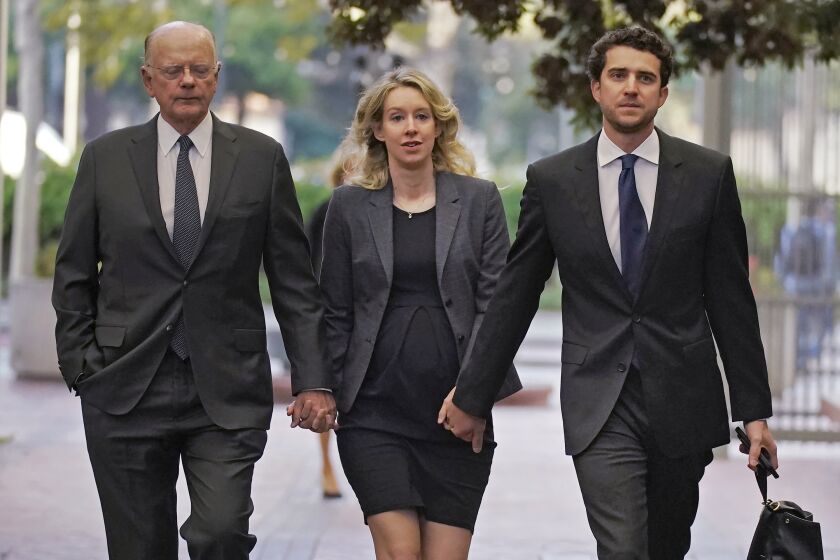 FILE - Former Theranos CEO Elizabeth Holmes, center, arrives at federal court with her father, Christian Holmes IV, left, and partner, Billy Evans, in San Jose, Calif., Monday, Oct. 17, 2022. In a motion filed Thursday, Jan. 19, 2023, in federal court in Northern California, federal prosecutors say Elizabeth Holmes is a flight risk and shouldn’t be allowed to stay out of prison while she appeals her 11-year prison sentence for defrauding investors. (AP Photo/Jeff Chiu, File)