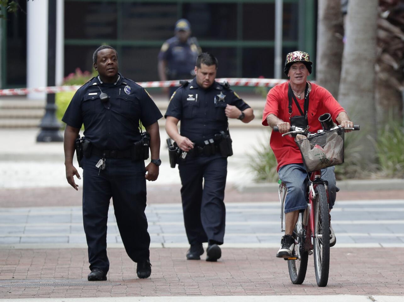 Police officers escort a bicyclist away from the scene of Sunday's shooting at the Jacksonville Landing, a riverfront mall in Jacksonville, Fla.