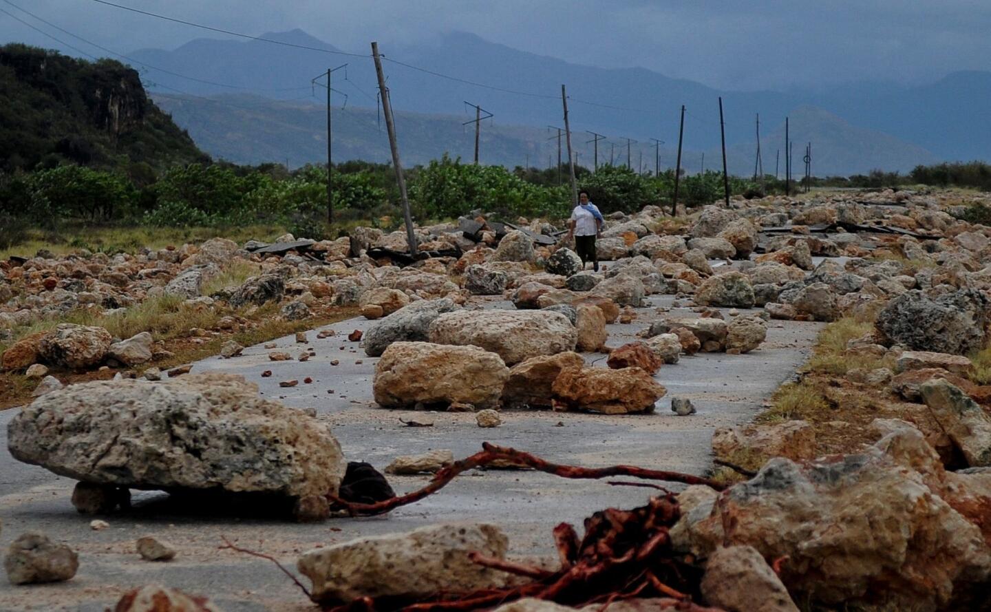 A woman walks Oct. 5, 2016, along a coastal road between Guantanamo and Baracoa, Cuba, that was left covered in rocks and severely damaged after the passage of Hurricane Matthew.